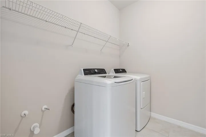 Clothes washing area featuring washing machine and dryer, baseboards, laundry area, and light tile patterned flooring