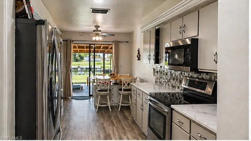 Kitchen featuring light cabinetry, stainless steel appliances, patterned tile backsplash, wood-finish flooring, and a breakfast bar with seating