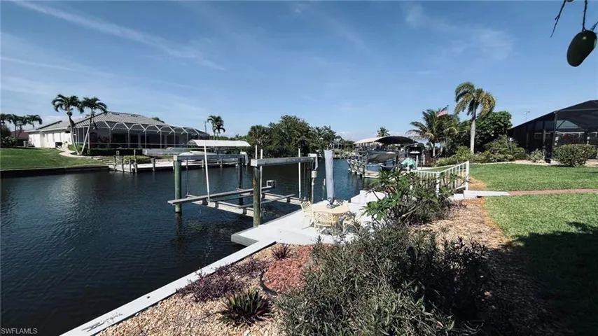 Waterfront property featuring a private boat dock with lift, concrete seawall, established landscaping, screened lanai, and mature palm trees