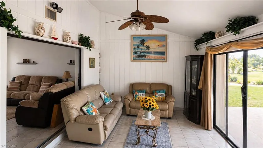 Living area featuring vaulted ceilings with a ceiling fan, white paneled walls, and tile flooring