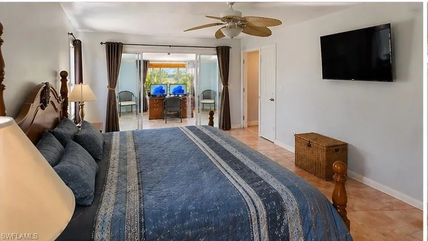 Bedroom featuring terracotta-style floor tiles, a ceiling fan, and sliding glass doors opening to an adjacent space with an exterior view