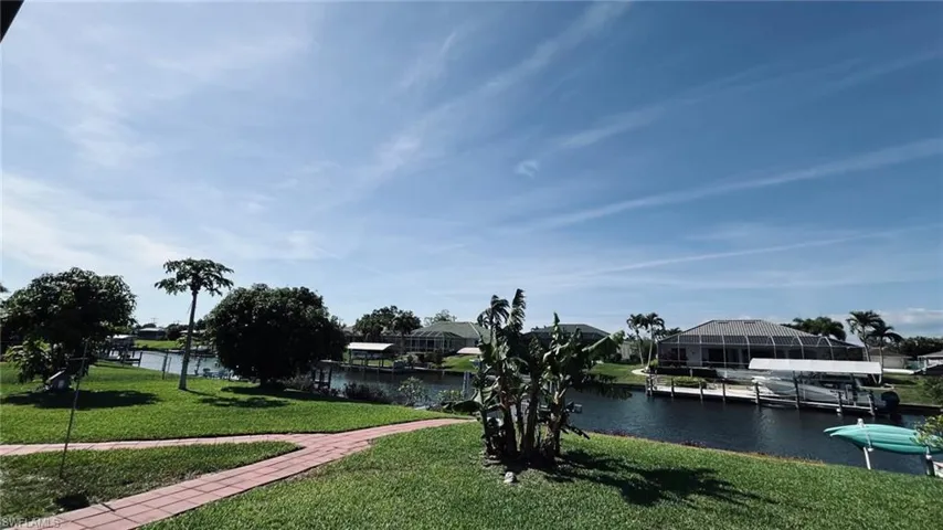 Waterfront property featuring a private boat dock with lift, canal access, a brick-laid pathway, mature landscaping, and a manicured lawn