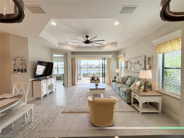 Living area featuring light tile patterned flooring, a ceiling fan, a tray ceiling, recessed lighting, and ornamental molding
