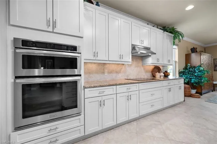 Modern kitchen featuring white shaker cabinetry, stainless steel double wall ovens, a coordinating cooktop with range hood, and light-toned patterned flooring