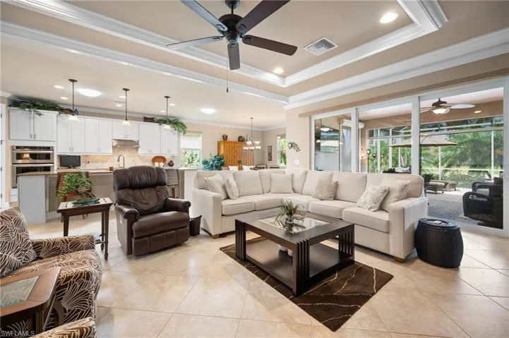 Open concept living area featuring tile flooring, crown molding, a ceiling fan, and sliding glass doors opening to a screened outdoor space