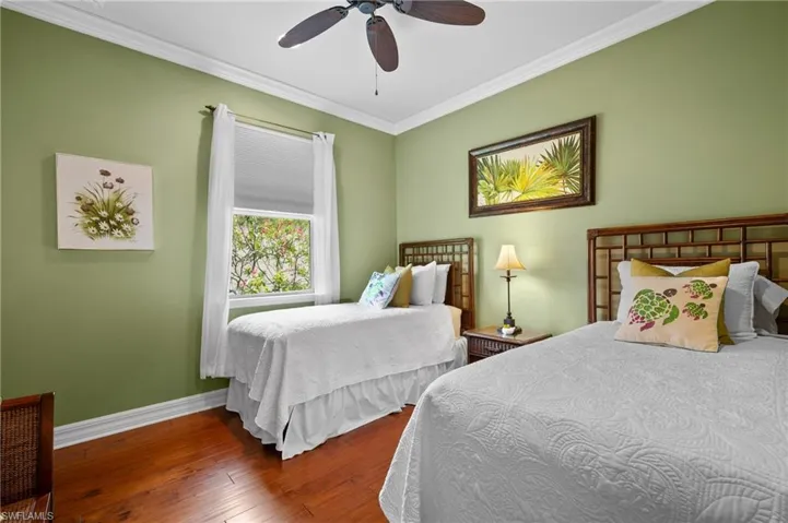 Warm wood-finish flooring provides a rich contrast to pale green walls in this room, featuring crown molding, a window with natural light, and a ceiling fan with integrated lighting