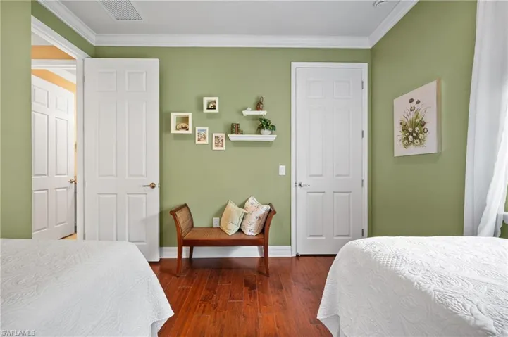 Interior space featuring wood-finish flooring, two white paneled doors with bronze hardware, and crown molding