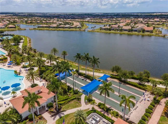 Expansive outdoor recreation area featuring a multi-lane bocce ball court, resort-style swimming pool, and a clubhouse with a terracotta tile roof