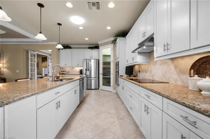 Expansive kitchen featuring a large central island with an undermount sink, white shaker-style cabinetry, stainless steel appliances, granite countertops, and a tiled backsplash