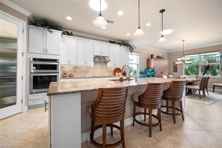 Spacious kitchen featuring white cabinetry, stone-finish countertops, stainless steel double ovens, and tile flooring