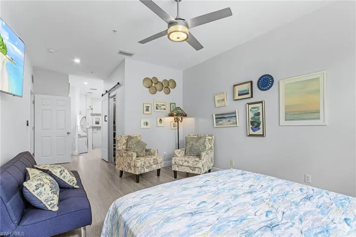 Bedroom featuring a barn door, wood finished floors, a ceiling fan, recessed lighting, and connected bathroom