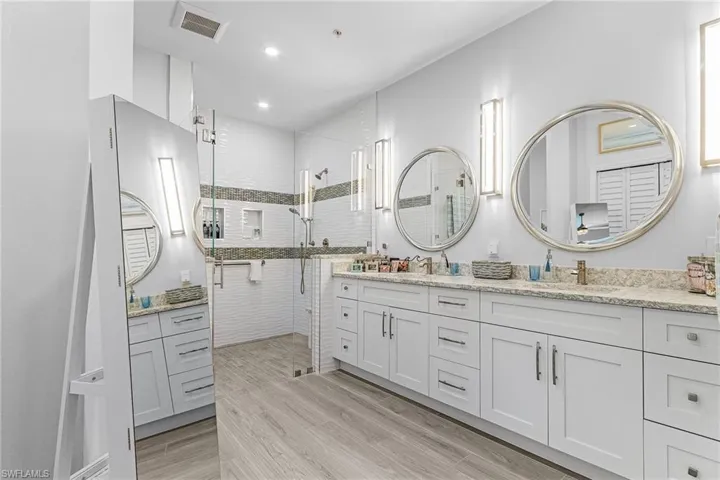 Full bathroom with double vanity, tiled shower, wood finished floors, and recessed lighting