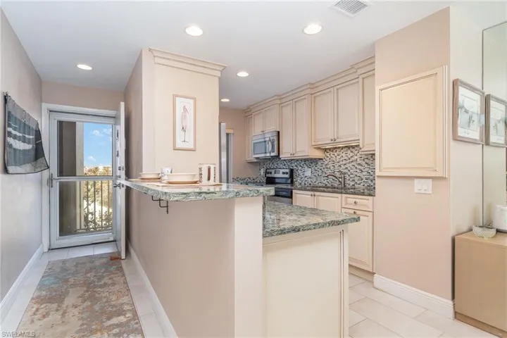 Kitchen featuring decorative backsplash, a kitchen breakfast bar, kitchen peninsula, stainless steel appliances, and cream cabinets