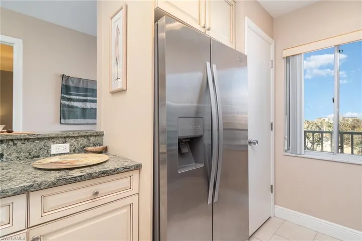 Kitchen featuring light tile patterned flooring, stainless steel fridge, cream cabinets, and dark stone countertops