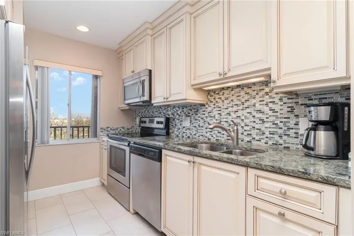 Kitchen with backsplash, dark stone counters, sink, appliances with stainless steel finishes, and cream cabinetry