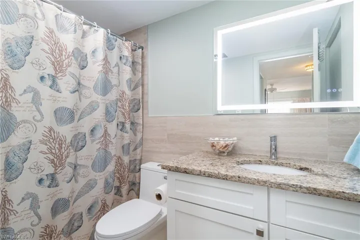Bathroom with a shower with curtain, vanity, ceiling fan, tile walls, and toilet