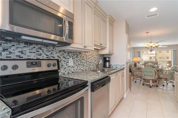 Kitchen featuring stainless steel appliances, an inviting chandelier, light stone counters, cream cabinetry, and light tile patterned floors