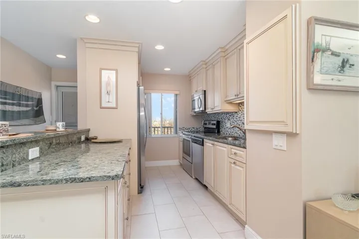 Kitchen featuring decorative backsplash, stainless steel appliances, sink, light tile patterned floors, and dark stone countertops