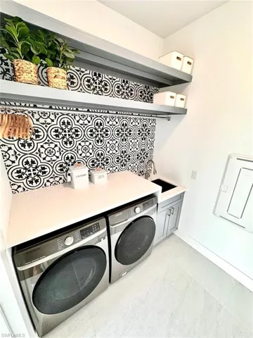 Clothes washing area featuring sink, cabinets, and washing machine and clothes dryer