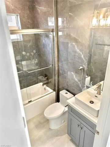 Full bathroom with toilet, tile patterned flooring, vanity, bath / shower combo with glass door, and tile walls