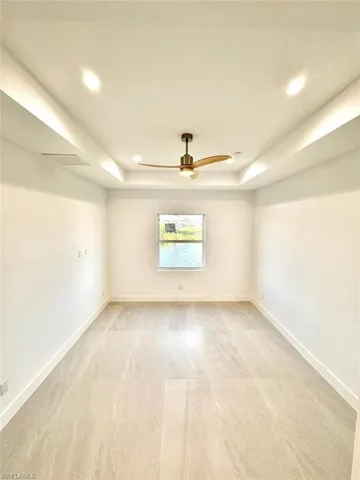 Carpeted empty room featuring ceiling fan and a tray ceiling