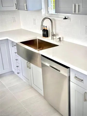 Kitchen featuring stainless steel dishwasher, backsplash, and light tile patterned floors
