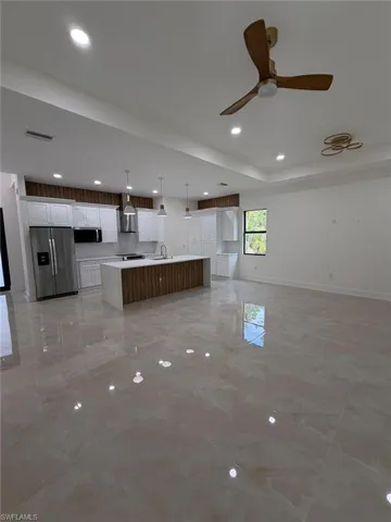Kitchen featuring open floor plan, white cabinets, appliances with stainless steel finishes, a large island with sink, and hanging light fixtures
