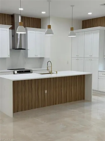 Kitchen with a spacious island, white cabinetry, wall chimney range hood, pendant lighting, and light stone countertops