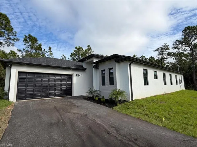 View of front of house featuring driveway, a front yard, stucco siding, and a garage