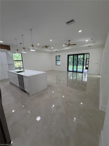Kitchen with hanging light fixtures, white cabinetry, a center island with sink, a ceiling fan, and light stone counters