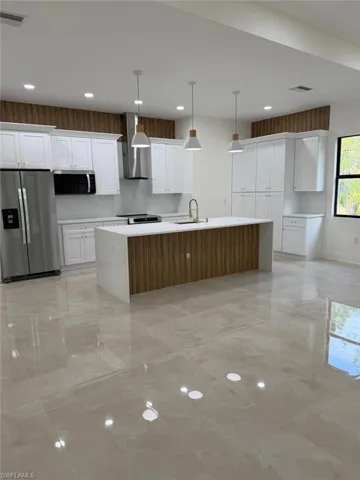 Kitchen featuring stainless steel appliances, white cabinetry, a kitchen island with sink, pendant lighting, and wall chimney range hood