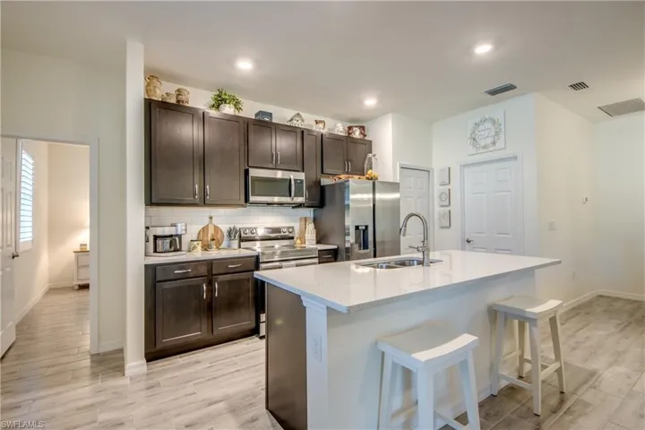 Beautiful white quartz countertops and dark cabinetry adorn this kitchen. Added features include the breakfast bar, stainless steel appliances, and a pantry. The primary bedroom is through the door on the left.