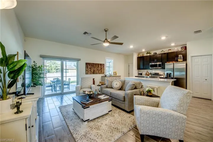 View of Great Room shows plank tile flooring (throughout home) and impact resistant sliding doors out to screened lanai and spool.