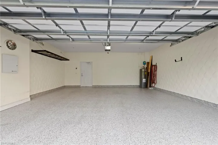 Spacious garage featuring a durable epoxy-finished floor, patterned wall textures, an integrated overhead storage rack, and interior door access. NEW HEAVY DUTY EPOXY FLOOR (2024), NEW HANGING STORAGE SHELVES (2021), NEW WATER HEATER (2016)