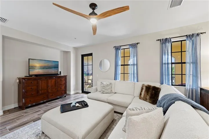 Spacious living area featuring wood-finish flooring, a modern ceiling fan, and multiple windows with dark frames. NEW TILE FLOOR (2018)