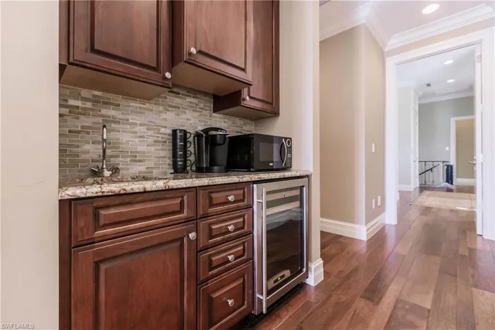 Bar with dark wood-type flooring, wine cooler, tasteful backsplash, light stone countertops, and ornamental molding