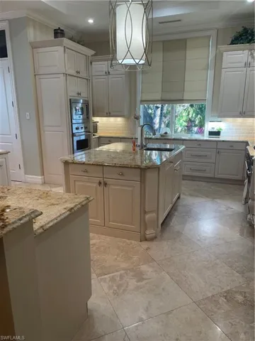 Kitchen with pendant lighting, an island with sink, sink, oven, and light stone countertops