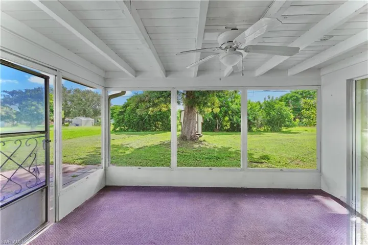 Unfurnished sunroom featuring beamed ceiling, ceiling fan, and view of scattered trees