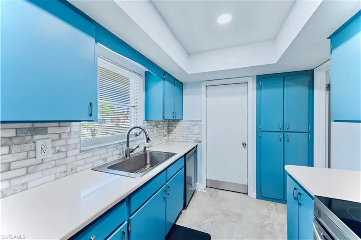 Kitchen featuring blue cabinetry, light countertops, black range with electric cooktop, decorative backsplash, and dishwashing machine