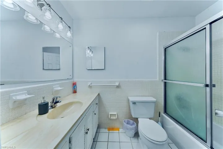 Full bathroom with light tile patterned floors, tile walls, vanity, enclosed tub / shower combo, and a wainscoted wall