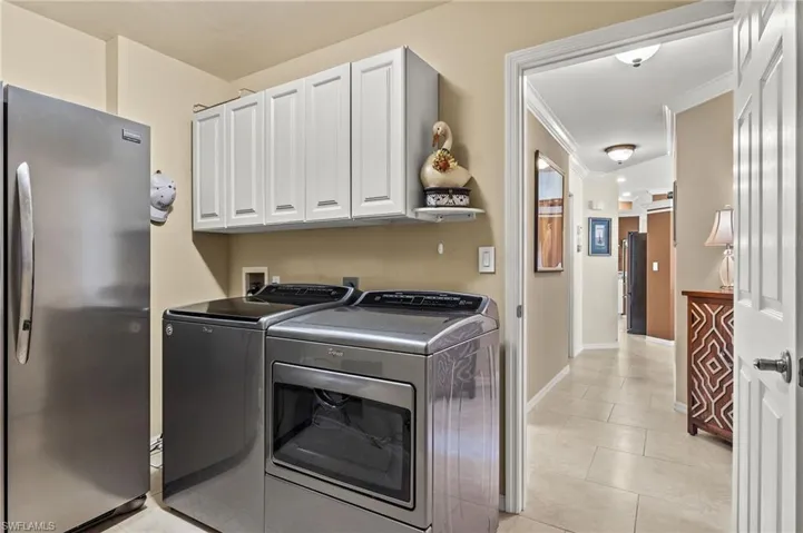 Laundry room featuring washing machine and dryer, cabinets, light tile patterned floors, and crown molding
