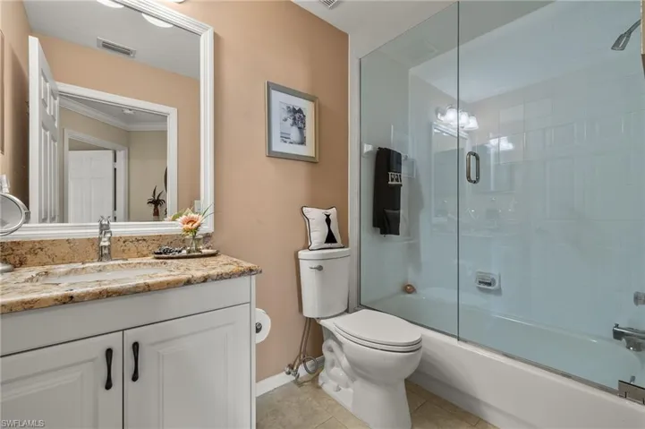 Full bathroom with tile patterned floors, ornamental molding, vanity, bath / shower combo with glass door, and toilet
