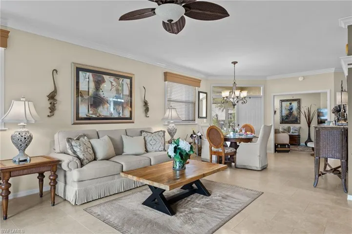 Living room with light tile patterned floors, ornamental molding, and ceiling fan with notable chandelier