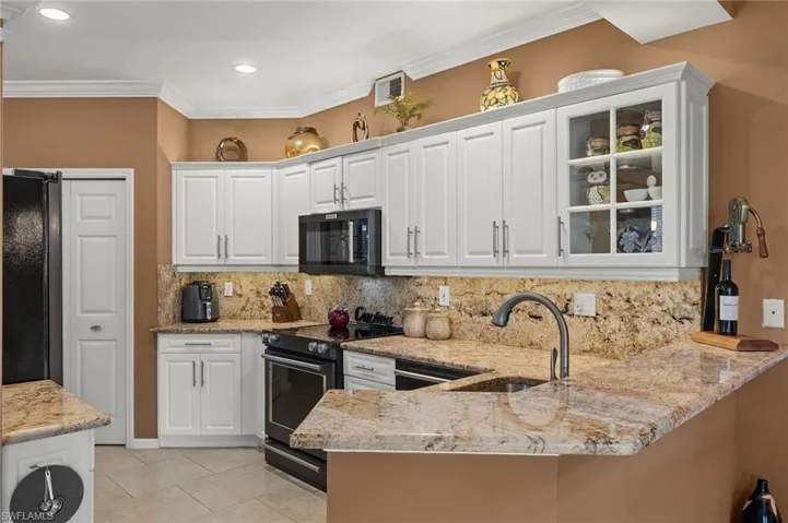 Kitchen with white cabinetry, sink, black appliances, light stone counters, and kitchen peninsula