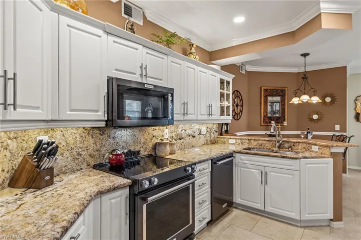 Kitchen featuring crown molding, appliances with stainless steel finishes, pendant lighting, white cabinets, and kitchen peninsula
