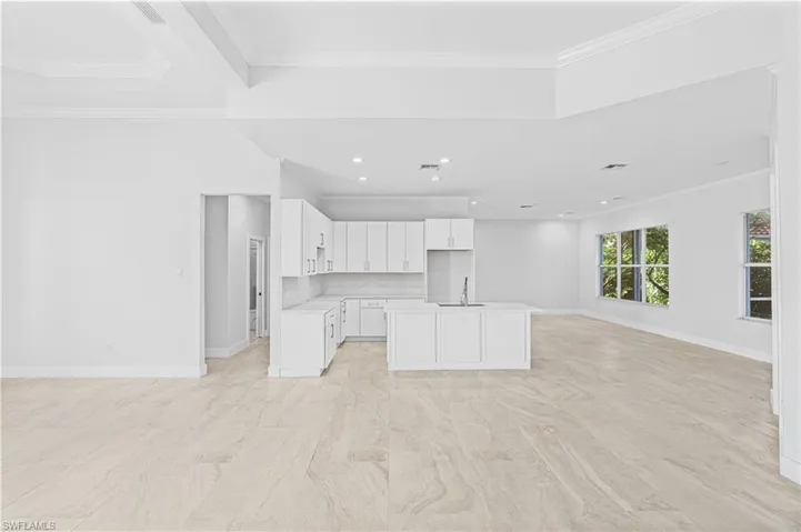 Kitchen with open floor plan, white cabinetry, light countertops, crown molding, and a center island with sink