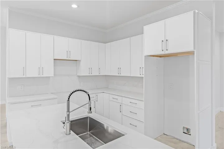 Kitchen featuring white cabinets, light stone counters, ornamental molding, tasteful backsplash, and recessed lighting
