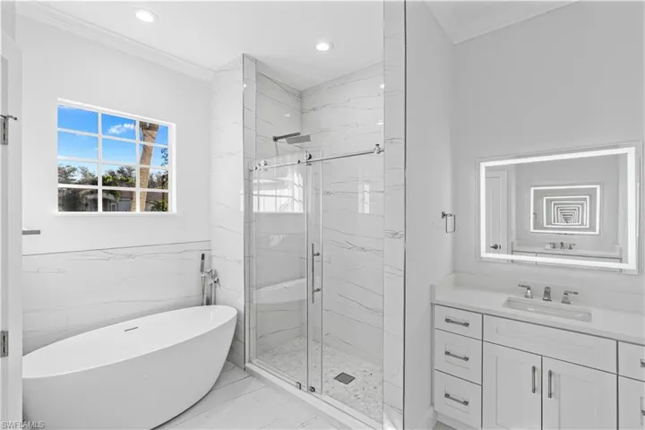 Full bath with ornamental molding, a marble finish shower, a freestanding bath, light marble finish flooring, and vanity