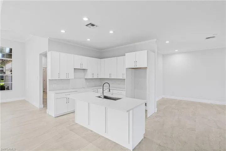 Kitchen with ornamental molding, white cabinets, backsplash, a center island with sink, and recessed lighting