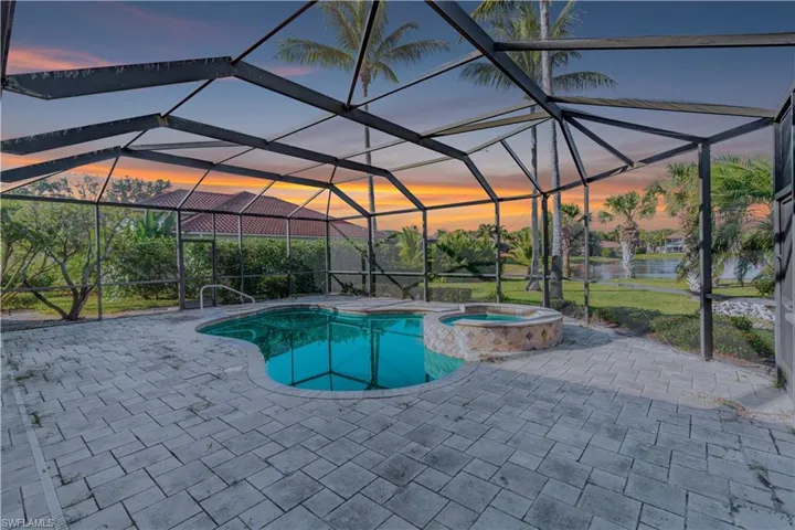 Pool at dusk featuring glass enclosure, a pool with connected hot tub, a sunroom, and a patio